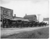 Une rangée de huit charrettes tirées par des chevaux, alignées devant le bâtiment de la boulangerie