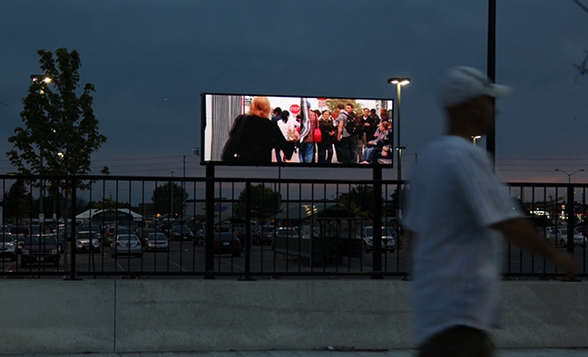 Image shows "Courants" video being displayed outdoors on an LED panel. A person is walking past it.