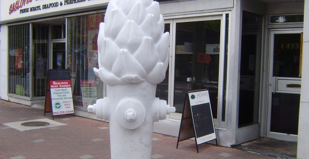 Image shows a sculpture of an oversized artichoke on top of a fire hydrant base and mounted on a plinth. 