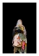 Un personnage dont le haut du corps est couvert d’articles vestimentaires de différentes couleurs se détache de l’arrière-plan noir. Le personnage porte des gants de tricot gris et tient trois roses blanches séchées devant son visage dissimulé sous des morceaux de tissus.