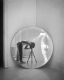 On aperçoit le reflet du photographe dans un miroir circulaire, l’appareil photo et le trépied étant au centre de l’œuvre. Le dos d’une sculpture figurative est également visible dans le reflet du miroir.