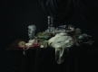 A photograph of various bits of plastic, fibre and cloth. Objects shown include a plastic water bottle, red frisbee, a plastic cup and a white cloth. These objects sit on a dark wooden table with a black tablecloth. Black curtains in the top right corner. The background is a black wall.