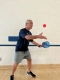 Don, inside a gym, throwing a pickleball into the air with one hand and holding a paddle with his other hand.