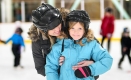 An adult hugs a child while skating with other families at an ice rink.