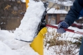 A close-up of a person clearing snow away from a yellow fire hydrant using a black shovel.