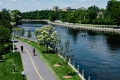 The Rideau Canal on a sunny day with paddlers on the water and a jogger and cyclist on a multi-use pathway.