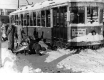 Ice-covered streetcar stuck in snow surrounded by men with shovels.