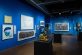 Galerie au murs bleu foncé remplis d'œuvres d'art 2D et 3D dans divers médias.