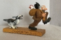 Humorous hand carving of a dog chasing a man clutching a chicken in a sack thrown over his shoulder.