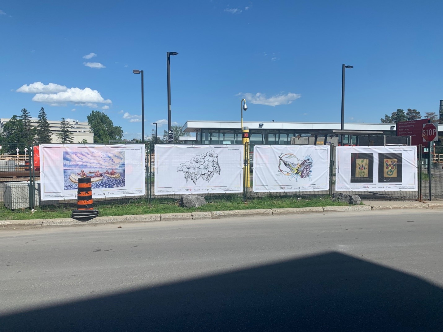 Artwork hanging on construction fencing in front of a public pathway