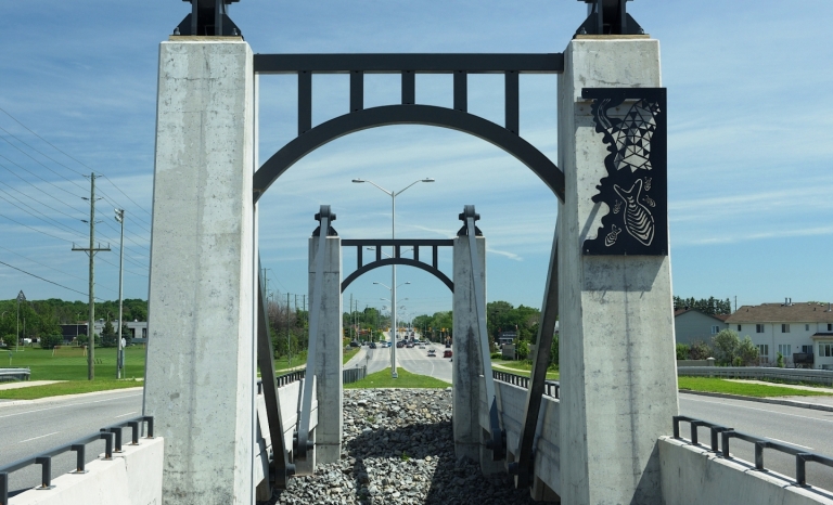 Arches de béton. L’une d’elles est ornée d’un panneau d’aluminium gravé de poissons et de formes abstraites.