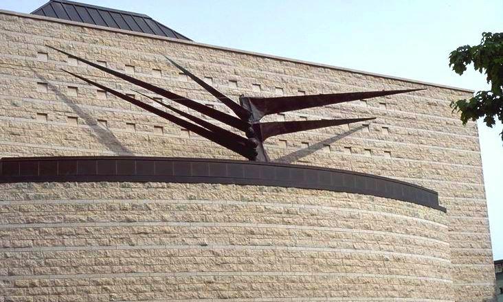 Sculpture abstraite avec de grandes branches métalliques triangulaires s’étendant d’un noyau central au sommet d’un bâtiment