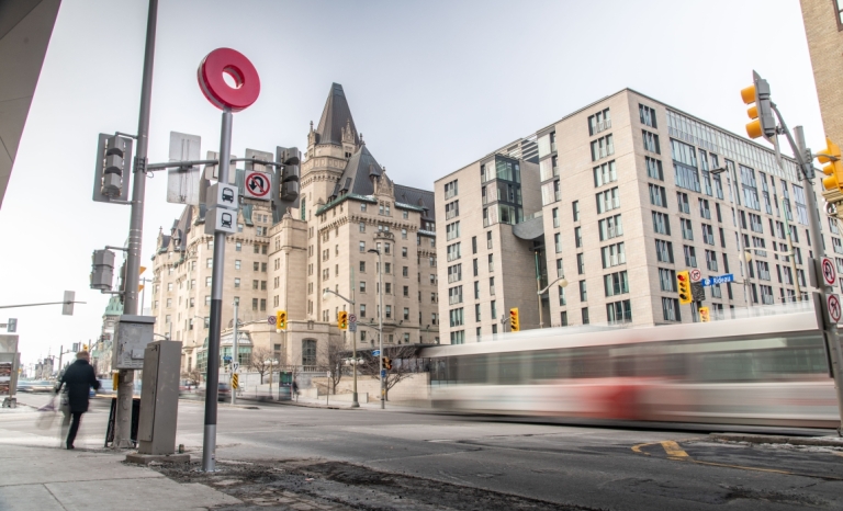 The corner of Rideau and Sussex with a moving bus, LRT sign post and the Chateau Laurier