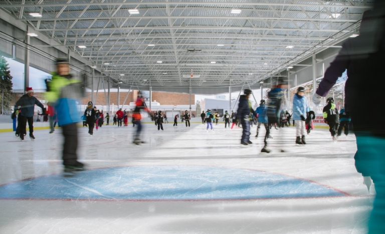 A crowd of skaters on the ice at a covered outdoor rink.