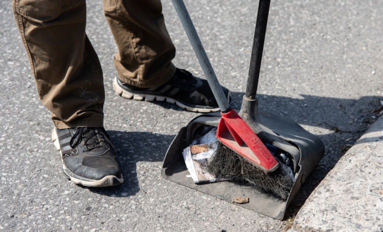 A worker sweeping litter from the street into a bucket dust pan