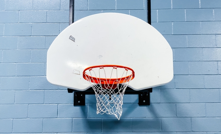 A basket ball hoop and backboard attached to a gym wall