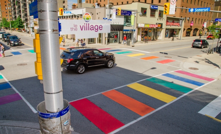 A rainbow painted cross walk in Centretown with a street sign that says "The Village"