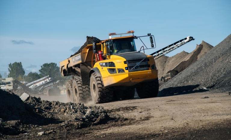 A large heavy dump truck full of soil driving through piles of sorted sand