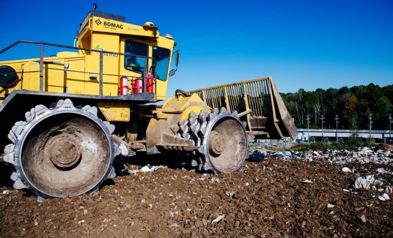 A close shot of a heavy bulldozer on top of a hill of waste