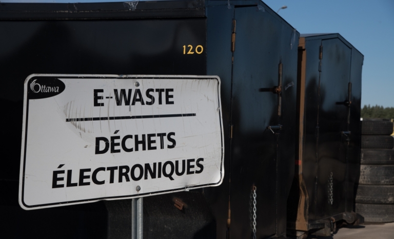 A sign that says "E-Waste" in front of large black containers