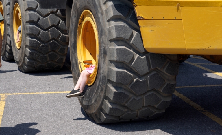 A close-up of a large wheel. A child is sitting inside the wheel rim, their legs visible.