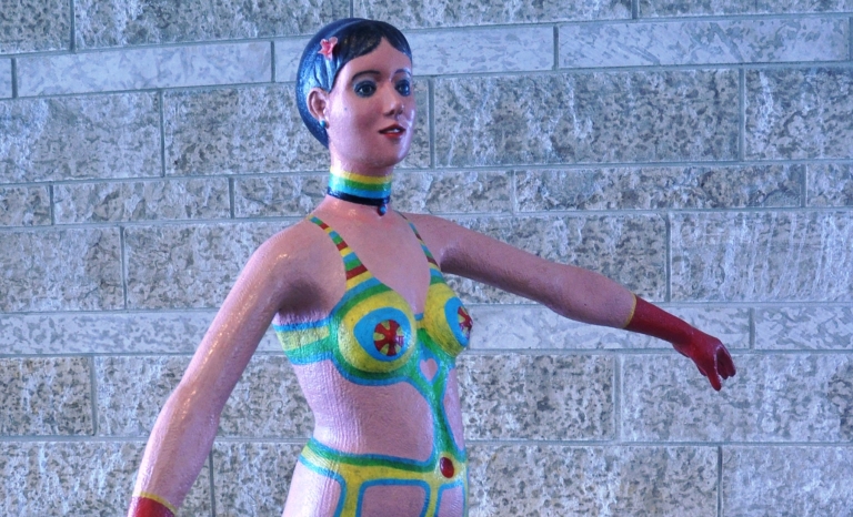 A painted plywood sculpture of a woman's torso and legs.
