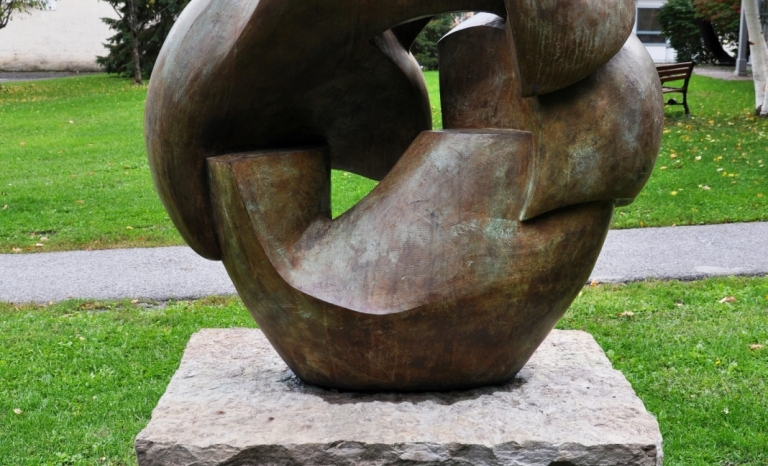 An image of a bronze sculpture in a broken circular form on a stone plinth.