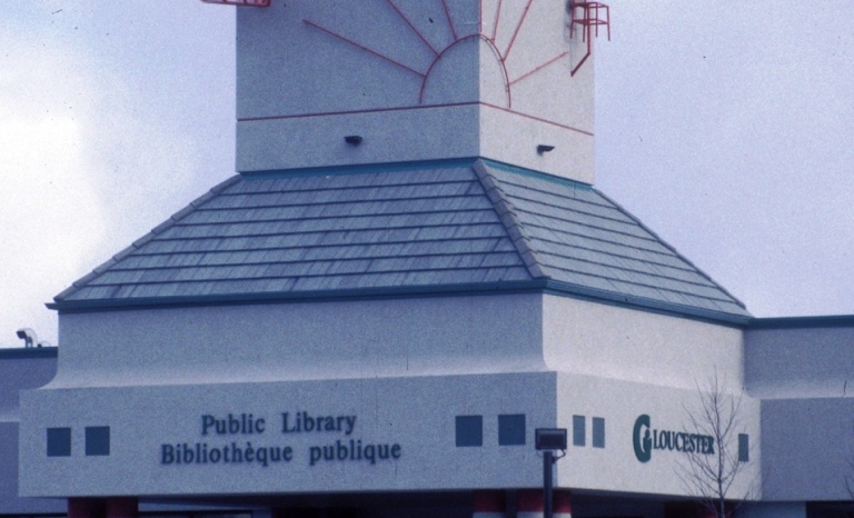 Image shows the red steel sculpture atop the library depicting the sun, a chair, and other objects along with the French word "decouvrir" meaning "discover".