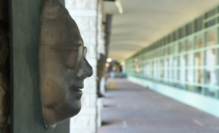 A bronze casting of a bespectacled man's face on the side of a wall.