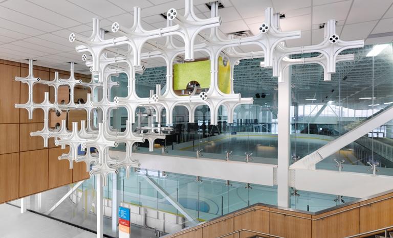 White modular sculptures made of tubing to form a grid hanging outside an indoor hockey rink