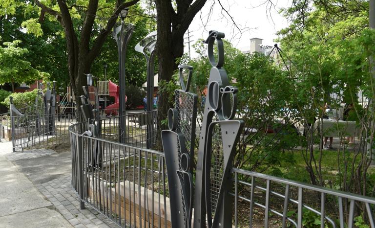 Fence consisting of clusters overlapping steel human shapes at the entrance of a park