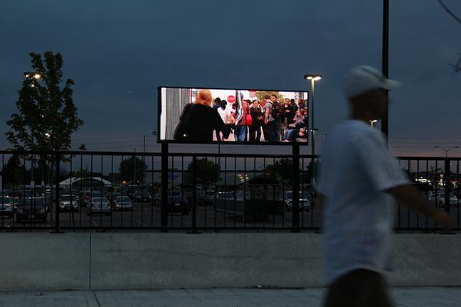 Image shows "Courants" video being displayed outdoors on an LED panel. A person is walking past it.
