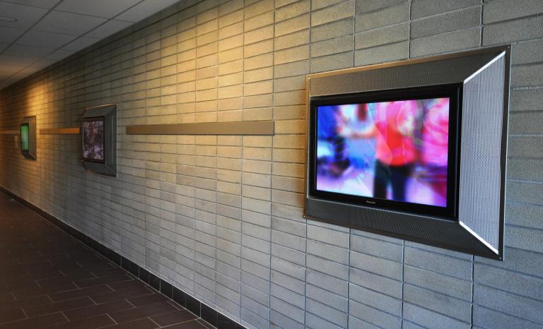 Photo depicting three LED screens installed on a wall, each depicting moving bodies.