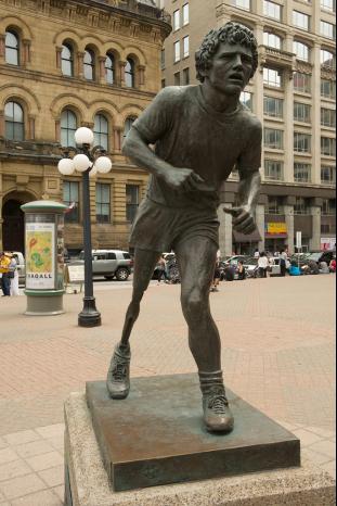 Sculpture of Terry Fox seemingly in motion, his strong right leg in front, his face and lagging artificial leg emphasize the struggle of the movement.