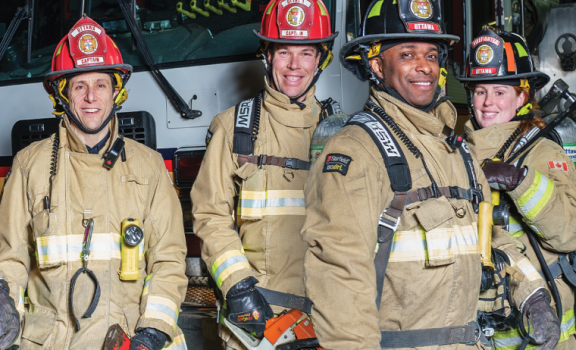 Quatre pompiers volontaires avec leur équipement de protection individuelle, debout devant un camion de pompier.