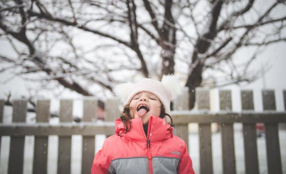 Young girl catching snow flakes with tongue