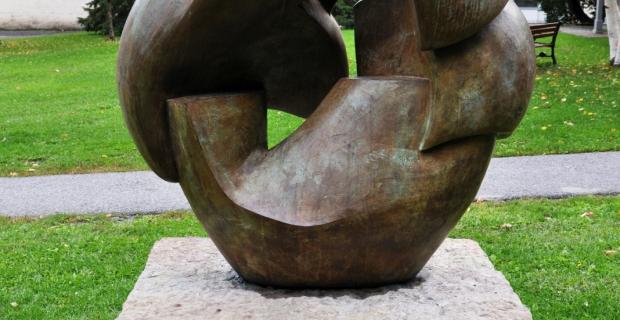 Une image d'une sculpture en bronze de forme circulaire brisée sur un socle en pierre.