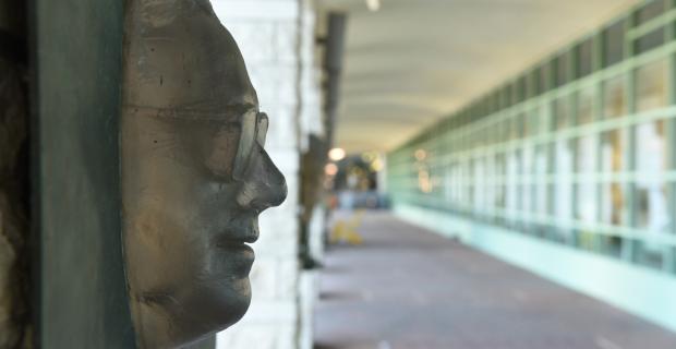 Moulage en bronze du visage d’un homme à lunettes accroché sur le côté d’un mur.