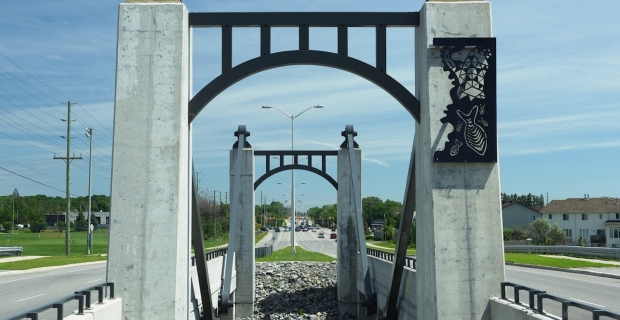 Arches de béton. L’une d’elles est ornée d’un panneau d’aluminium gravé de poissons et de formes abstraites.