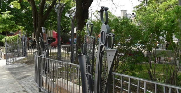 Clôture composée de grappes chevauchant des formes humaines en acier à l’entrée d’un parc