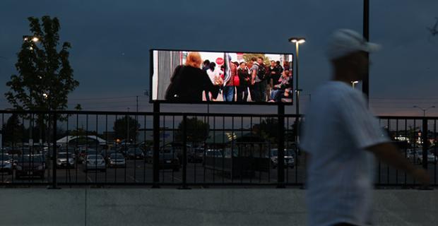 Photo de la vidéo « Courants » diffusée sur un écran DEL à l’extérieur. Une personne passe devant.