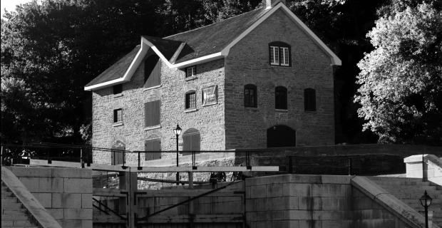 Image en noir et blanc d’un bâtiment en briques de trois étages sur la rivière.