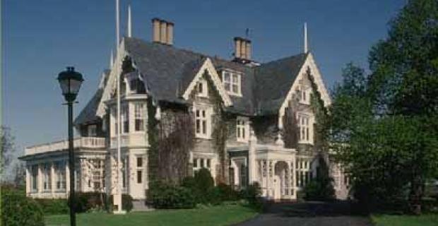 Villa avec des garnitures blanches, un toit gris et un grand arbre à l’avant. La résidence du haut-commissaire britannique au Canada.