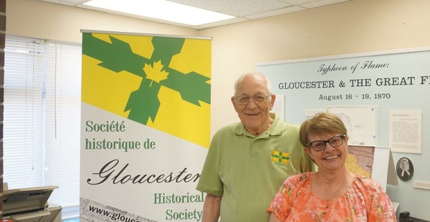 Two volunteers smile standing in front of a Gloucester Historical Society banner.