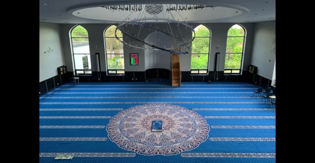 Main prayer hall with large windows, blue carpet and circular chandelier.