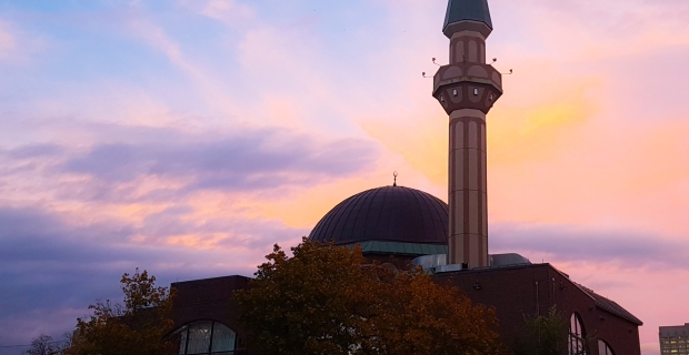 Exterior of a two-storey hall with raised minaret and central dome at sunset. 