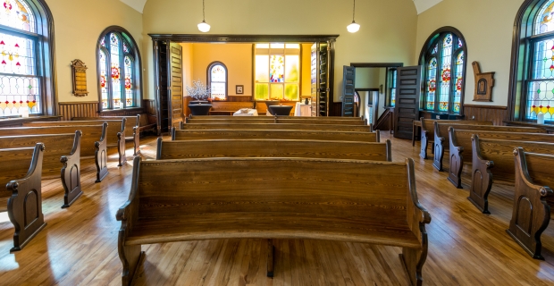 Pews fill a room with hardwood floors, yellow walls and stained glass windows. 