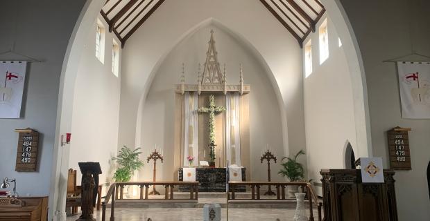 Un grand chœur avec des murs blancs, de hauts plafonds et une poutre en bois. La lumière naturelle pénètre par quatre hautes fenêtres. 