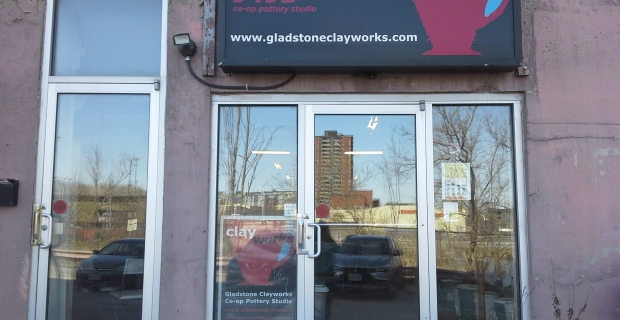 Entrée d’un bâtiment avec deux portes et fenêtres vitrées. Un grand panneau rouge et noir pour Gladstone Clayworks se trouve au-dessus de la porte.