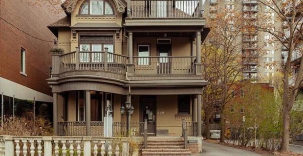 Une maison en briques brunes de trois étages avec un grand porche et des balcons un jour d’automne.